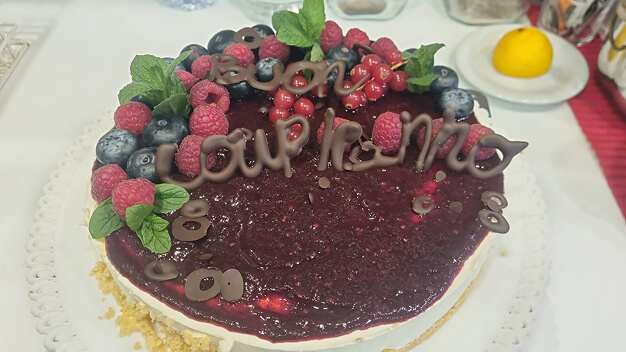 Torta con copertura ai frutti di bosco decorata con lamponi, mirtilli e scritta di auguri in cioccolato.