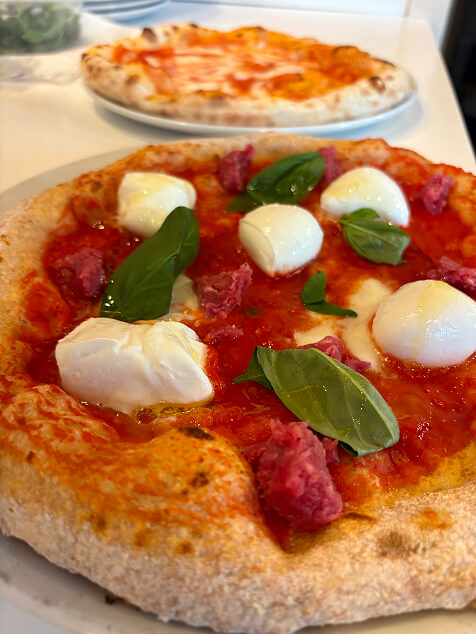 Sezione di pizza con cornicione alto e alveolato, con mozzarella fusa e pomodoro, su sfondo nero con logo del ristorante Il Sagittario.